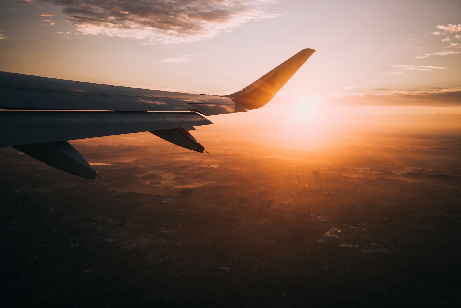 Airplane wing over a city at sunset, seen from a window seat
